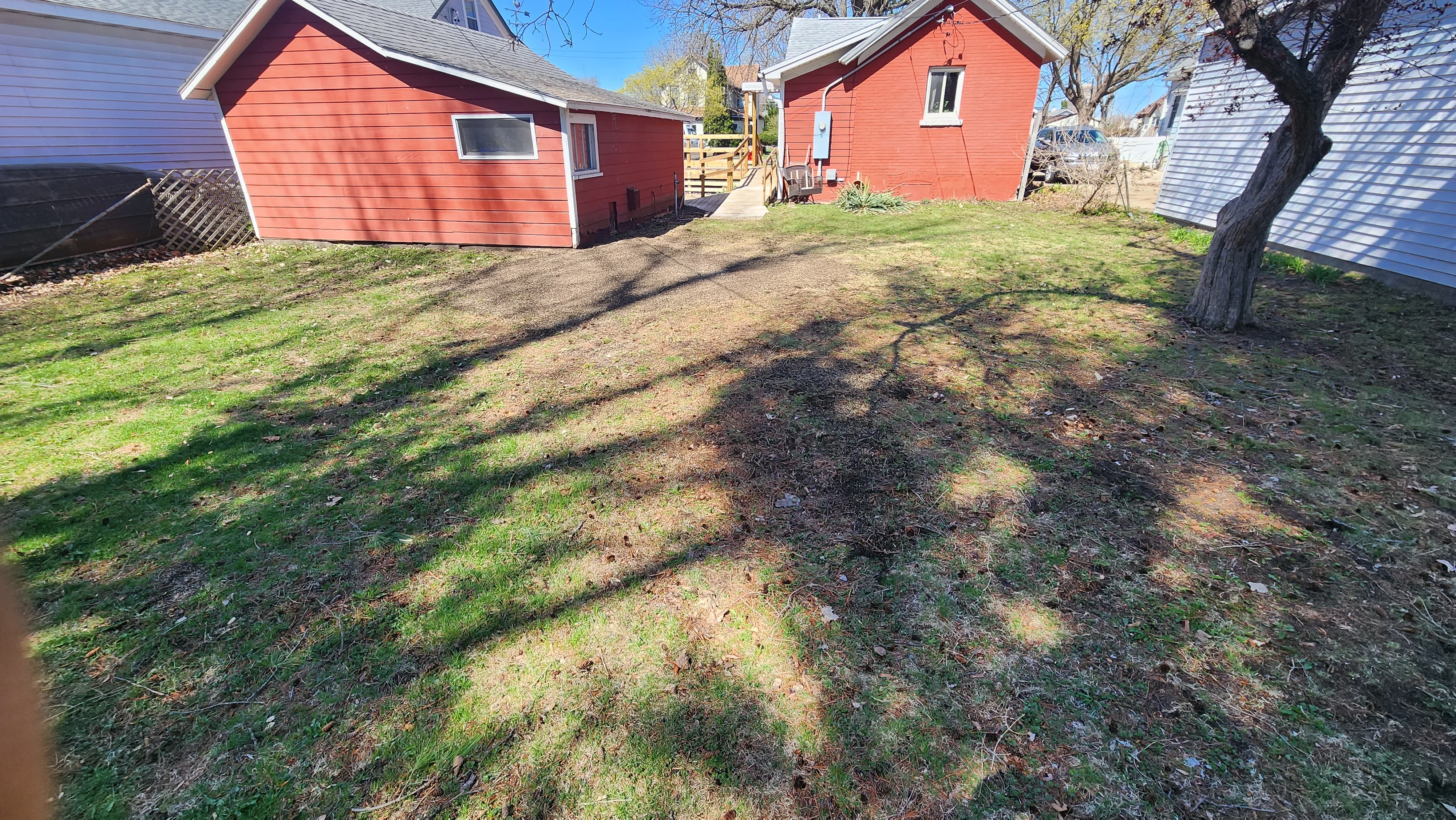 Cleared residential yard with tree stump removal and debris cleanup, red cottage visible