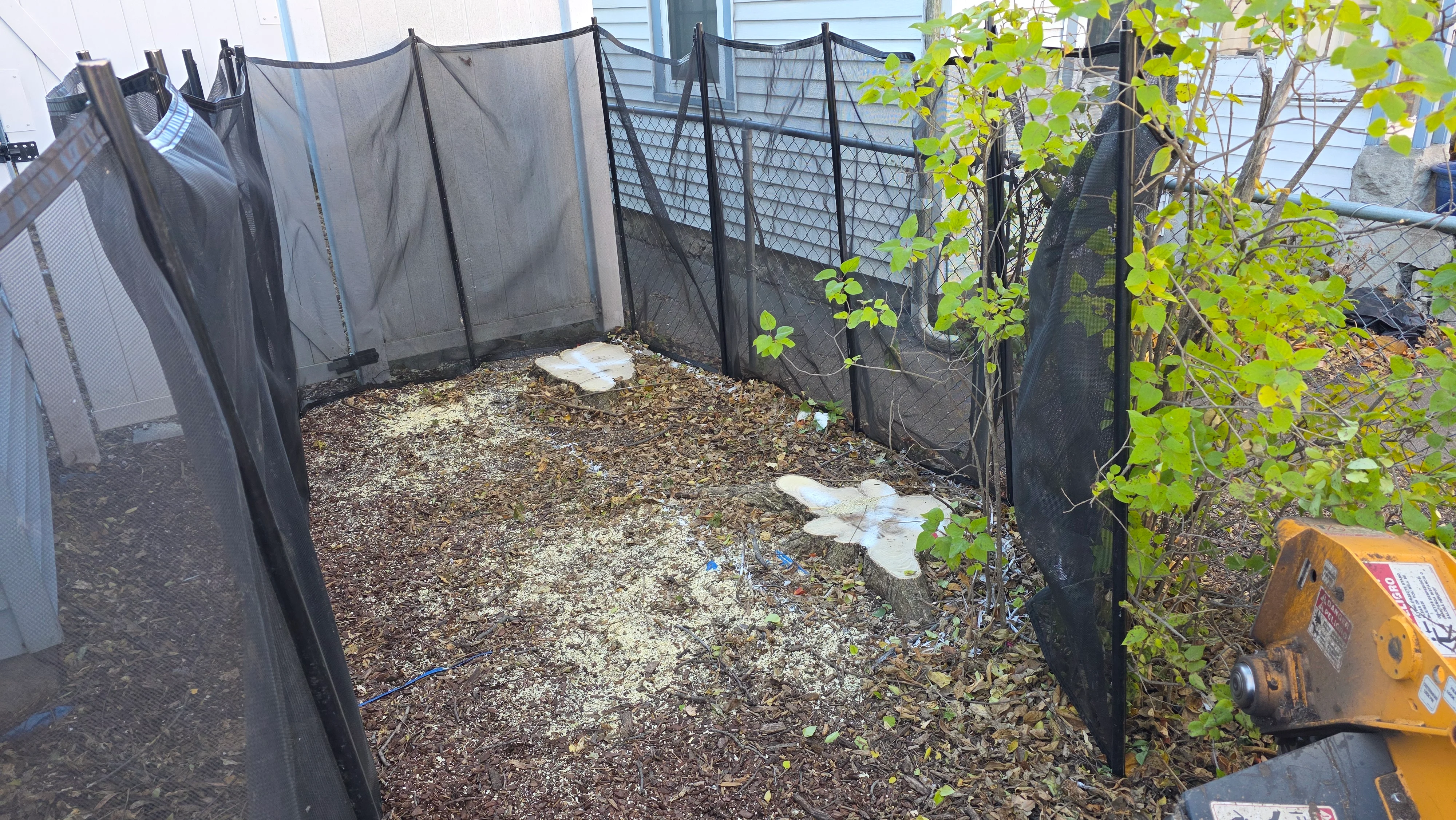 Enclosed yard with black mesh fencing, cleared wood chip debris, and landscape fabric installation