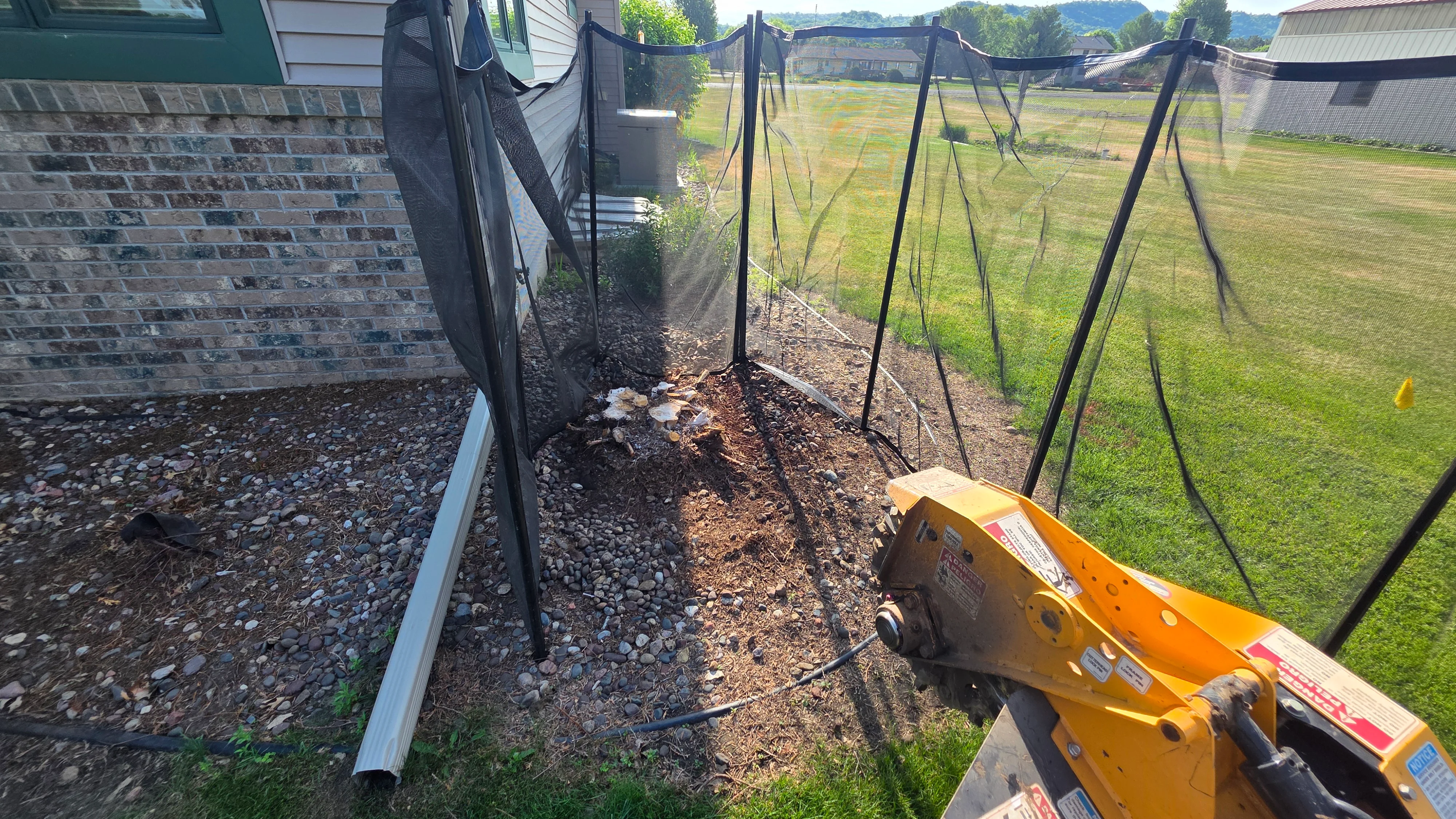 Tree removal site with stump grinder, cleared soil, and black landscape fabric installation