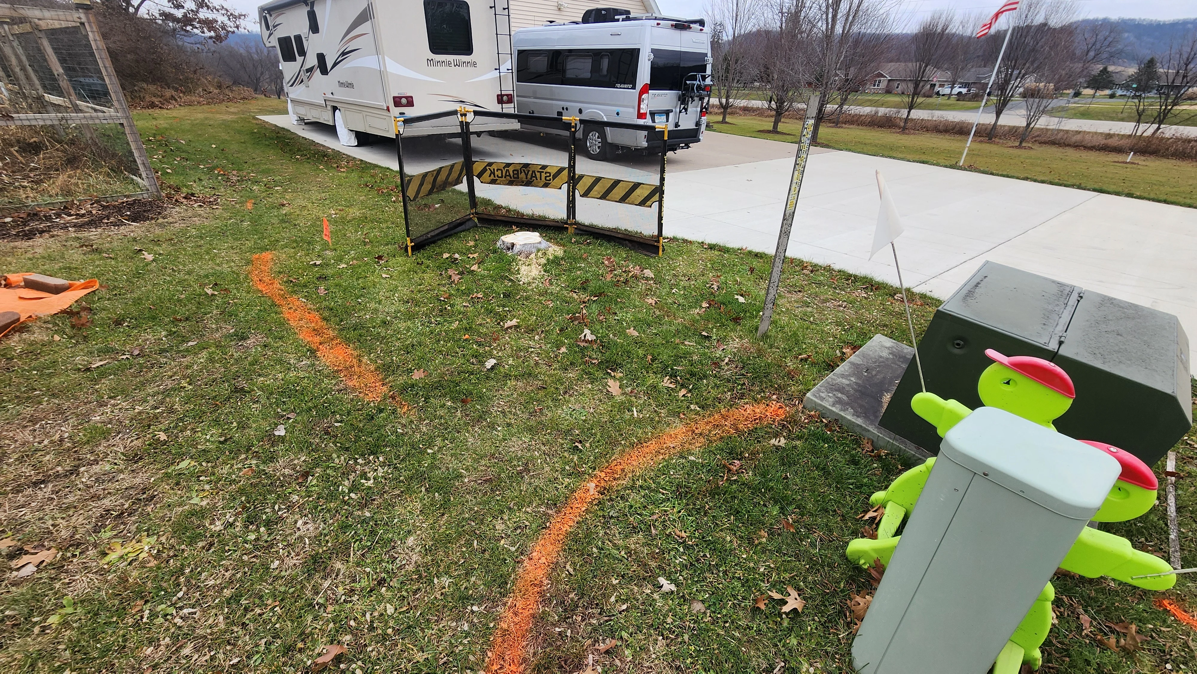 Orange utility line markings on grass with safety barriers and marked underground utilities
