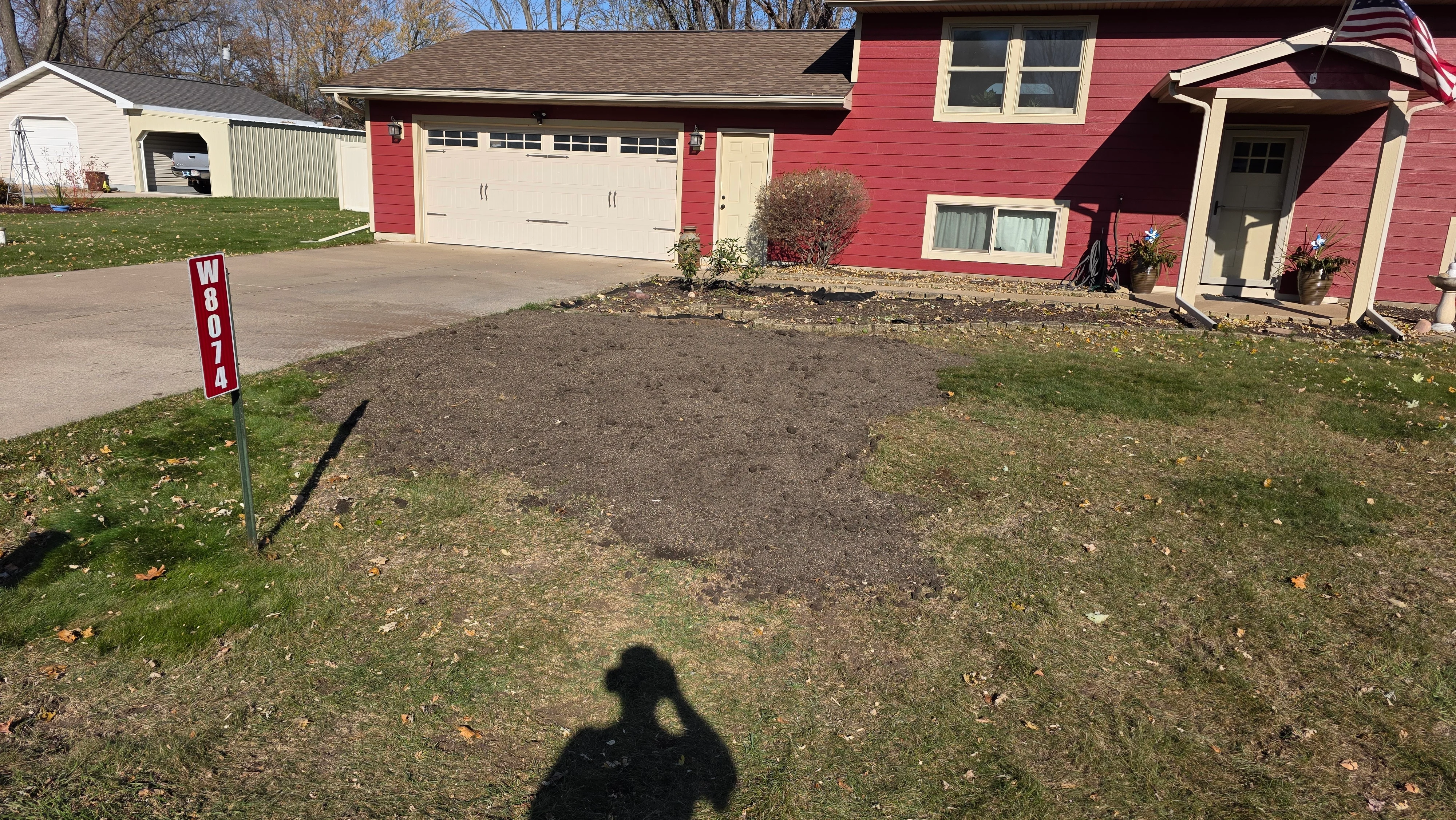 Cleared and graded residential lot with bare soil, adjacent to red house and garage