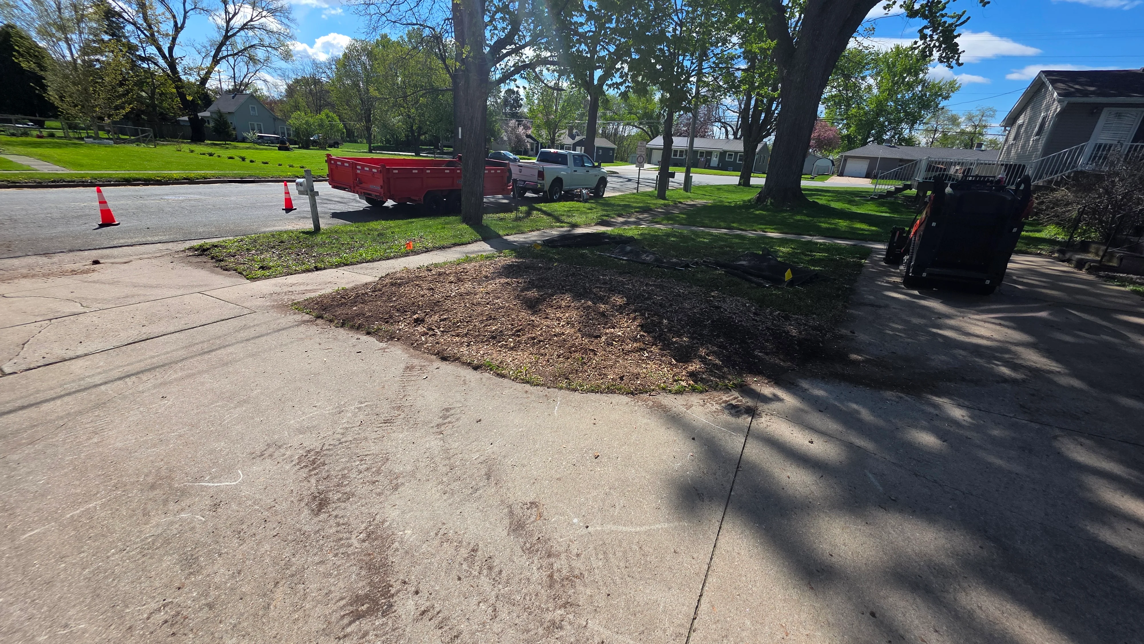 Tree removal site with fresh mulch, traffic cones, and cleared residential street