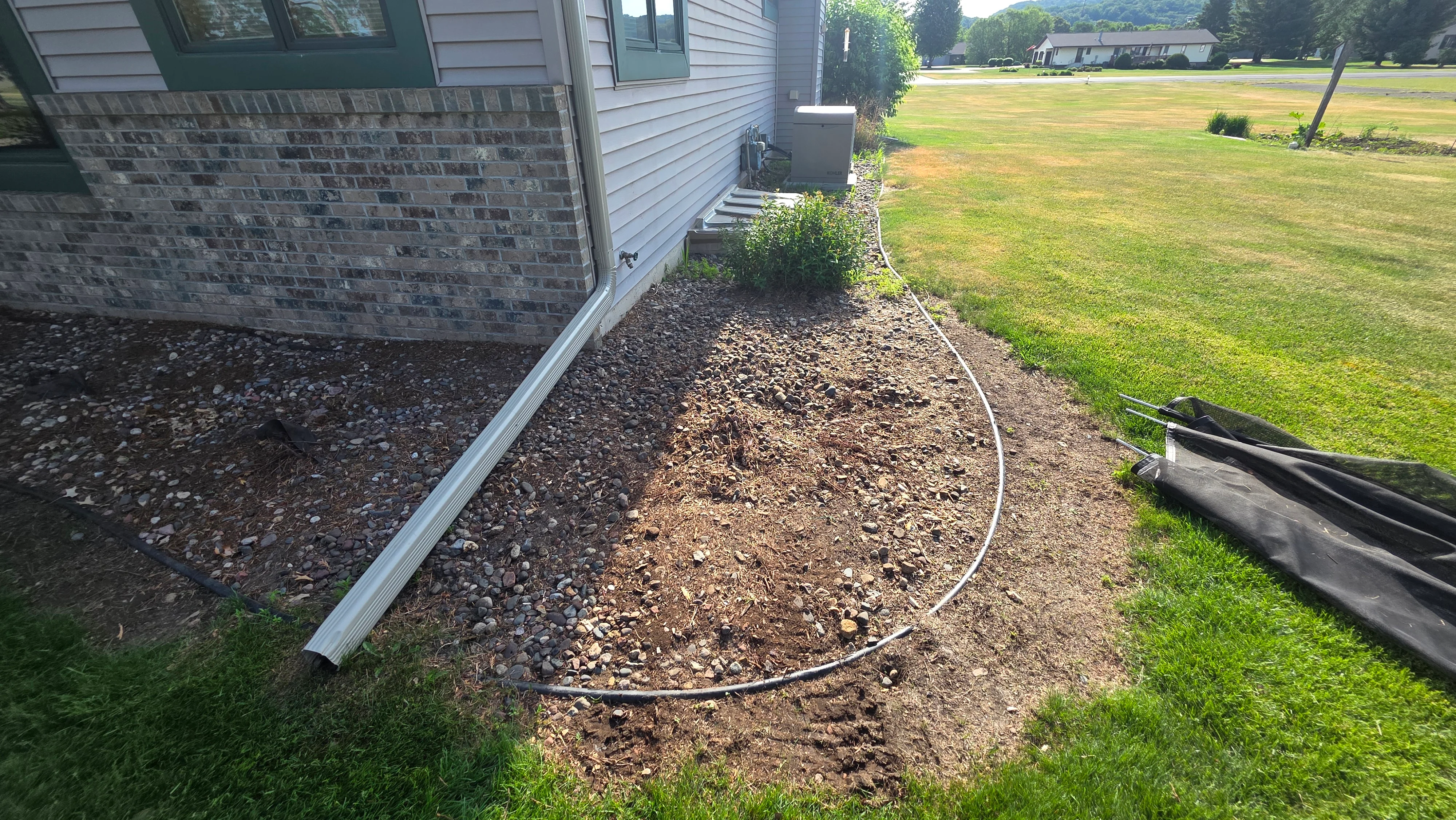 Foundation drainage bed with river rock, metal edging, and graded soil preparation
