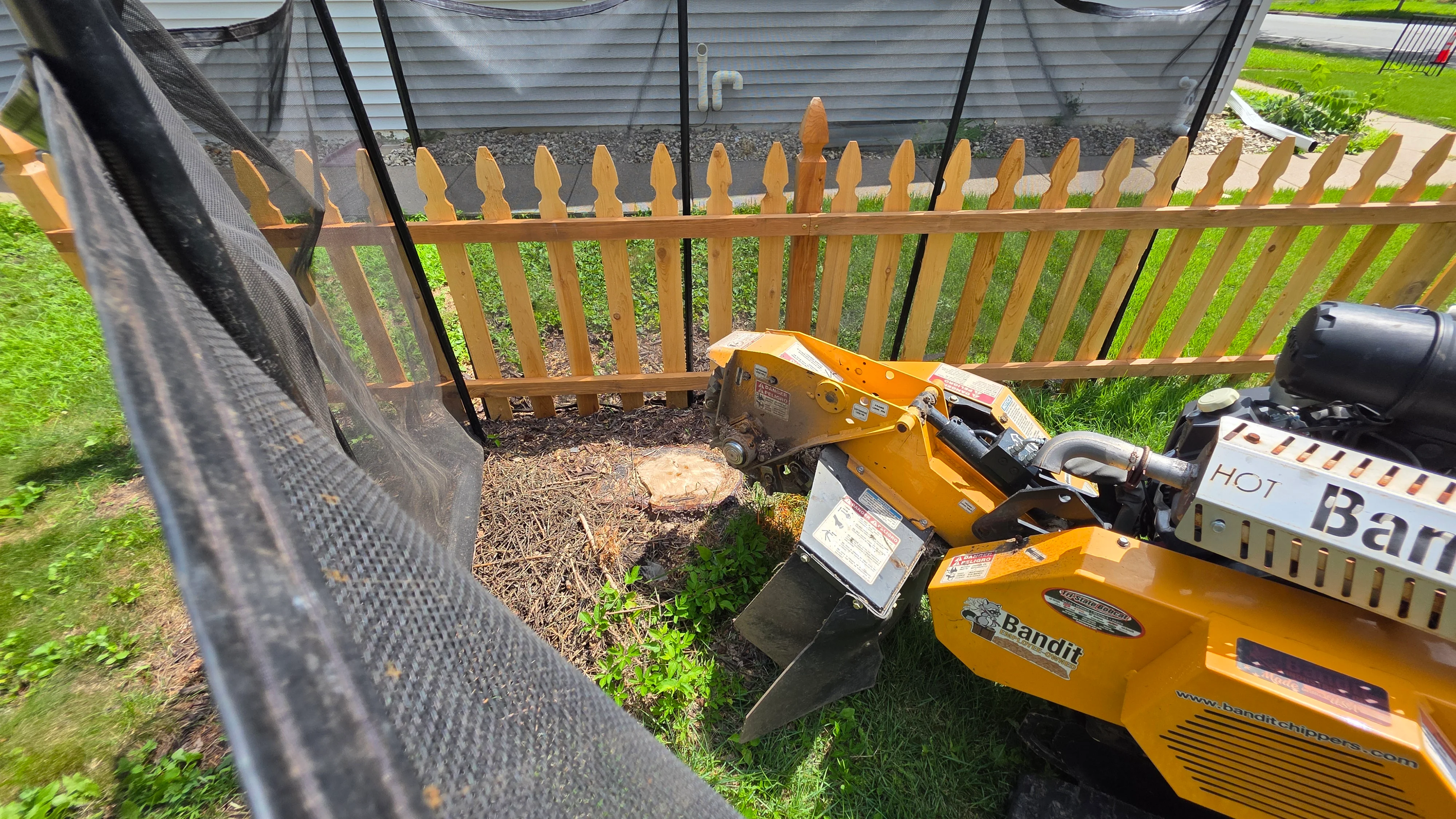 Bandit stump grinder and wood chipper equipment positioned in residential yard with wooden fence and mulch debris