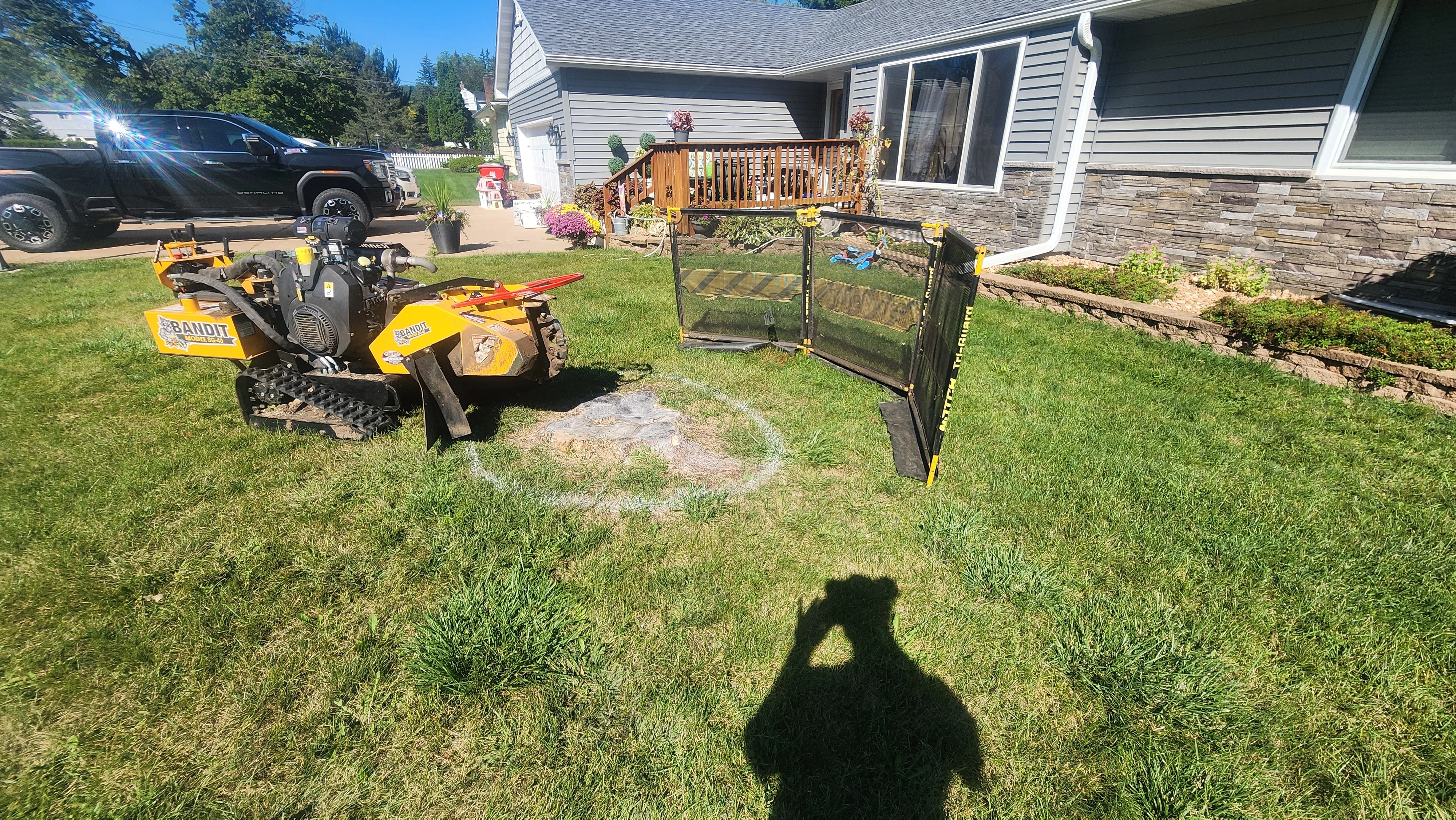 Tracked equipment and debris containment setup on residential lawn with fallen logs and yard waste