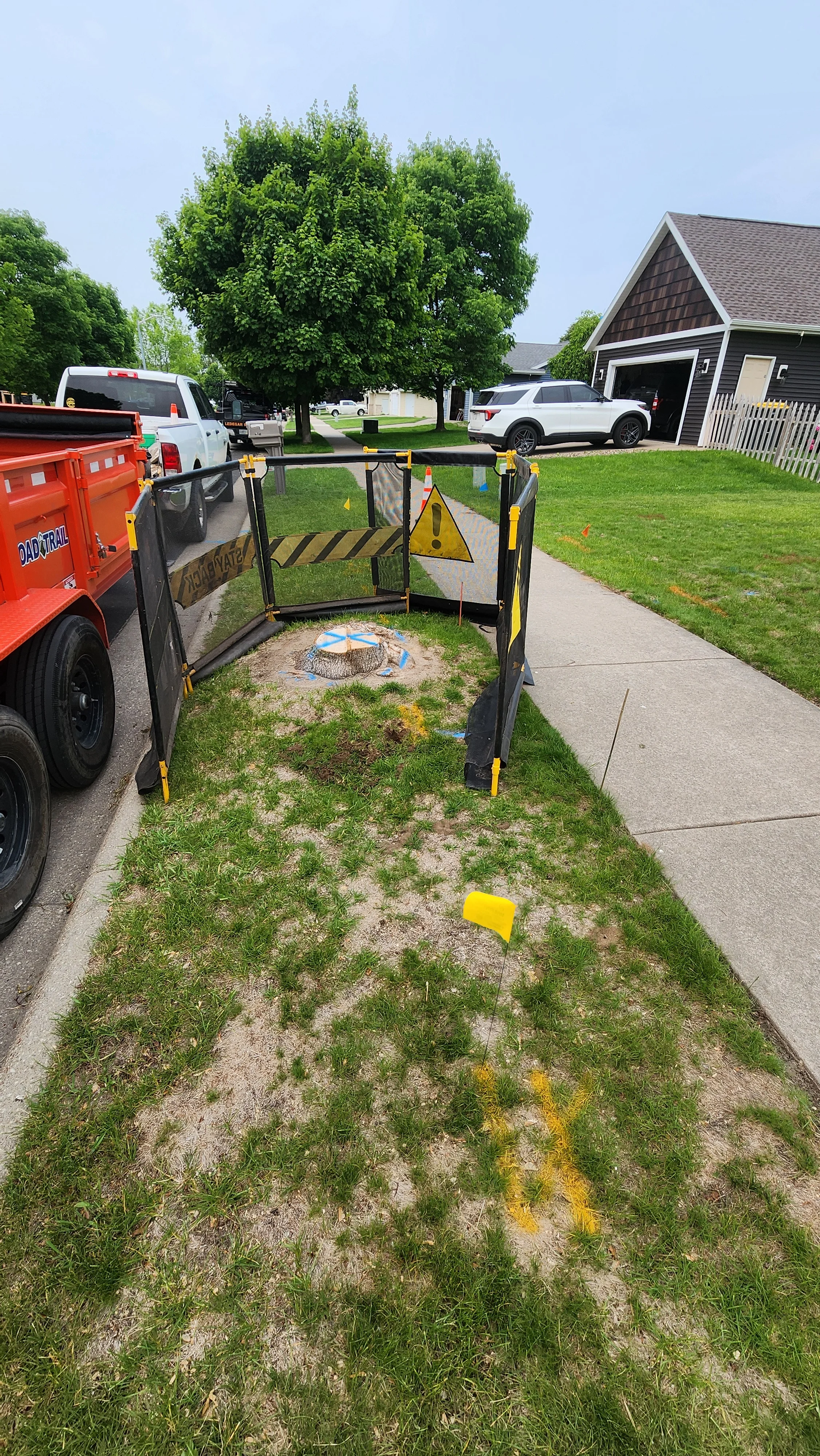 Tree stump removal with yellow and black safety fencing, protective barriers, and service truck on residential property