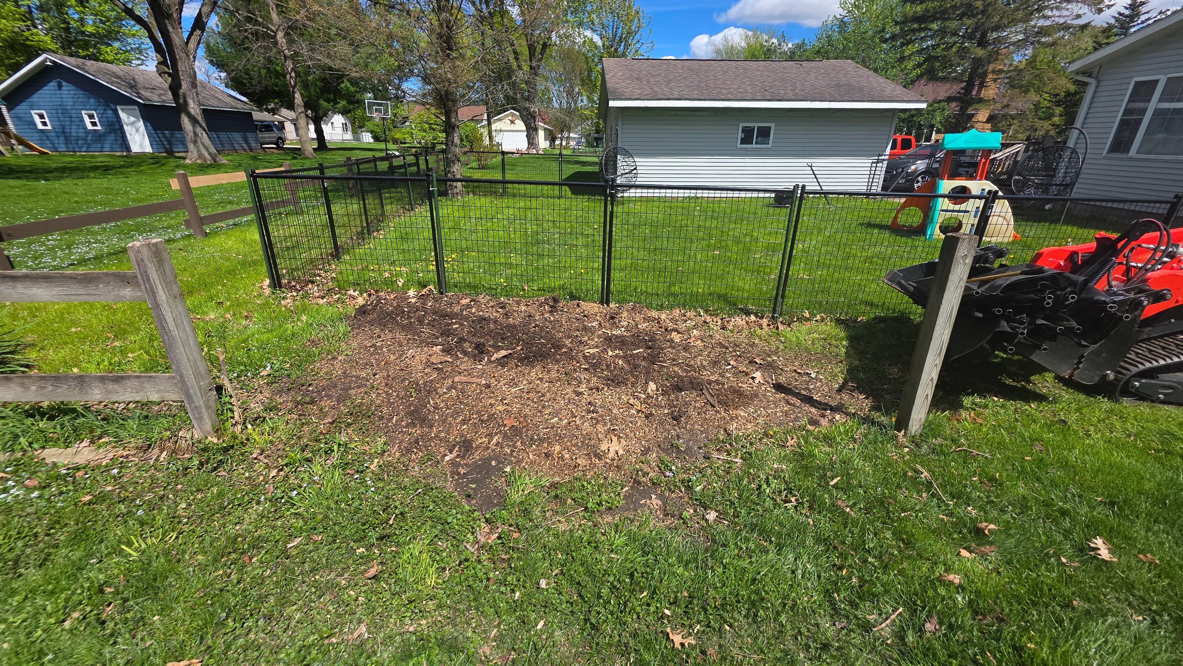 Black metal fence enclosure with wood chip mulch base and cleared yard area