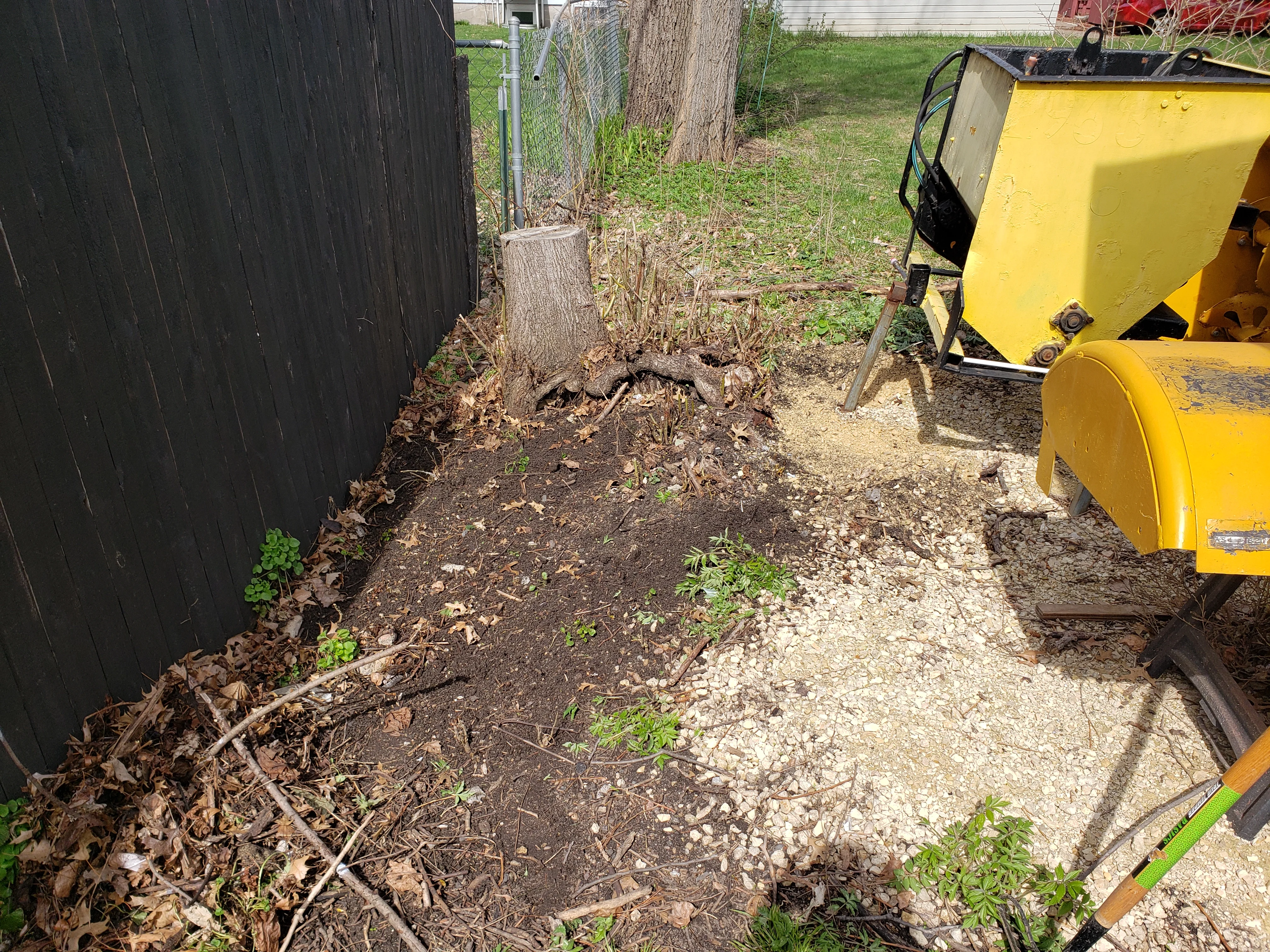 Stump grinding equipment and cleared debris area with gravel base next to black fence