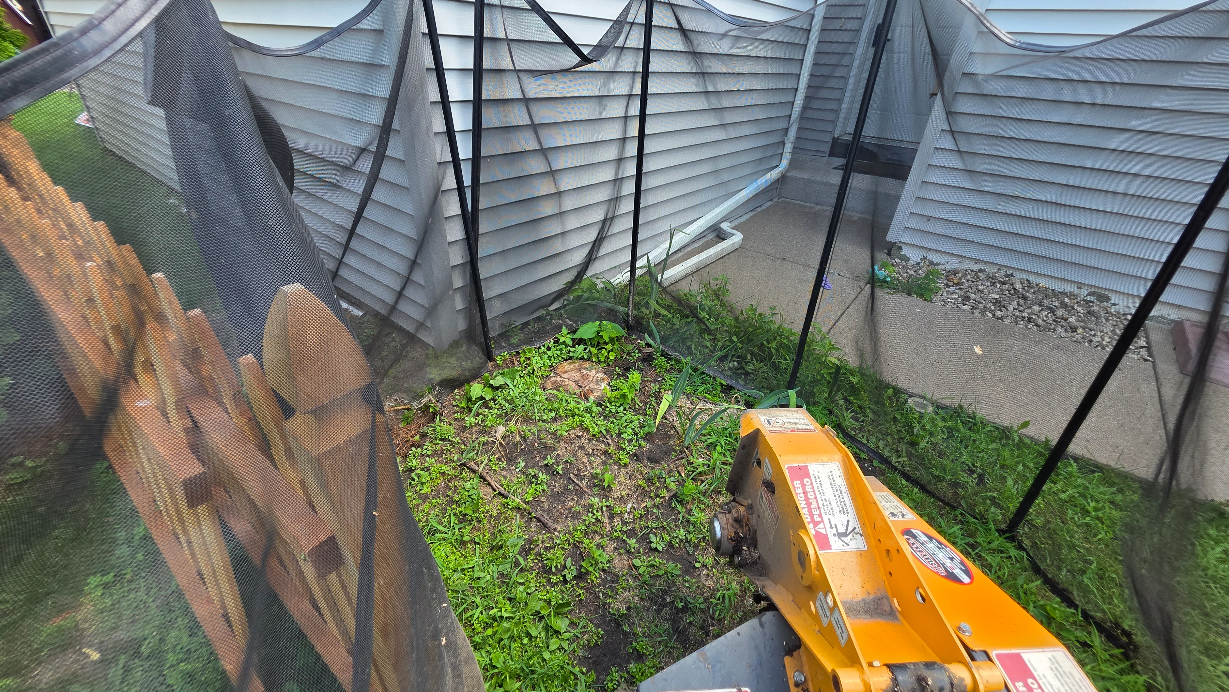 Cleared garden bed with removed weeds and debris, bordered by mesh fencing and vinyl siding