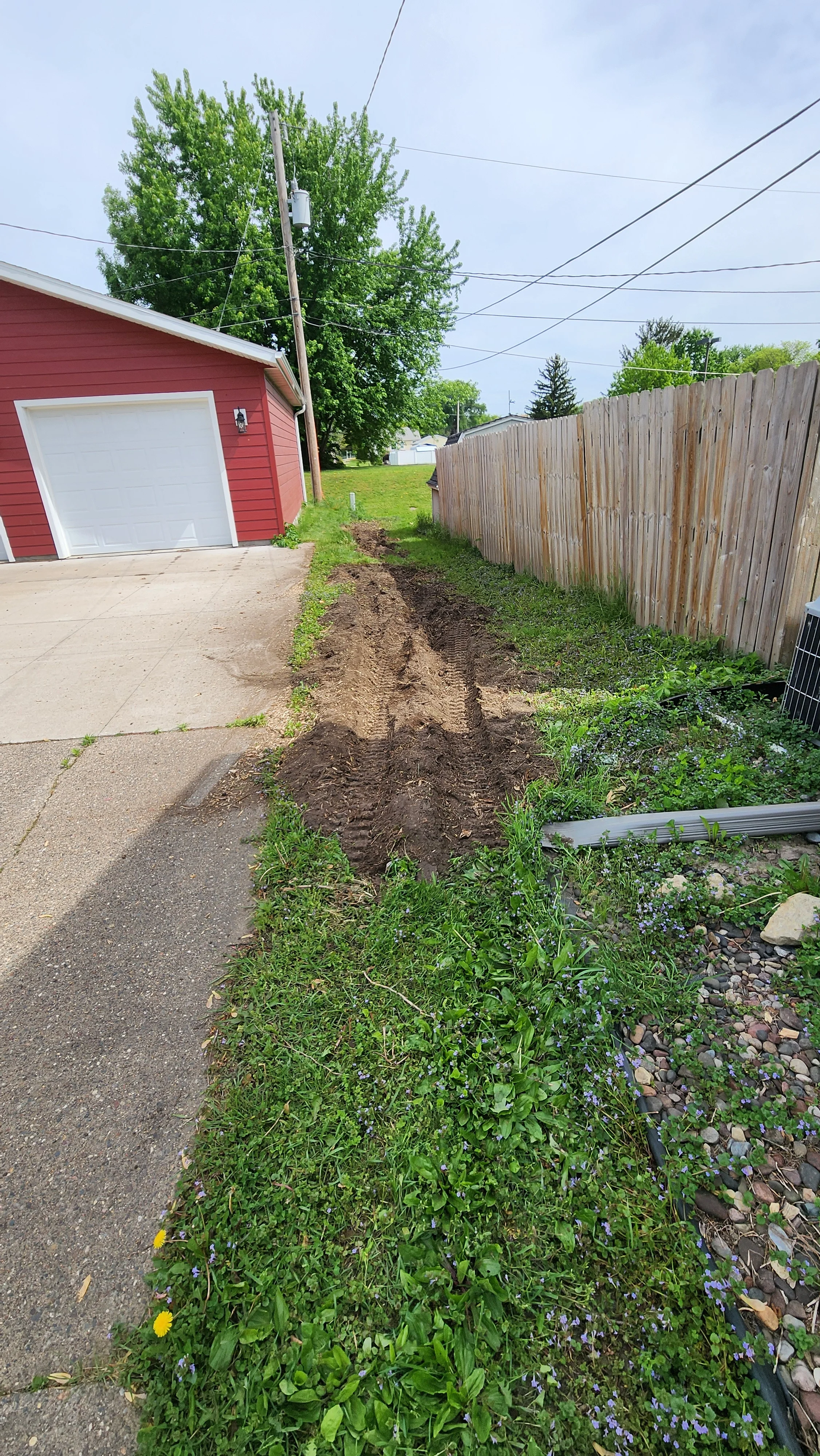 Cleared driveway with removed soil and vegetation debris next to wooden fence and red garage