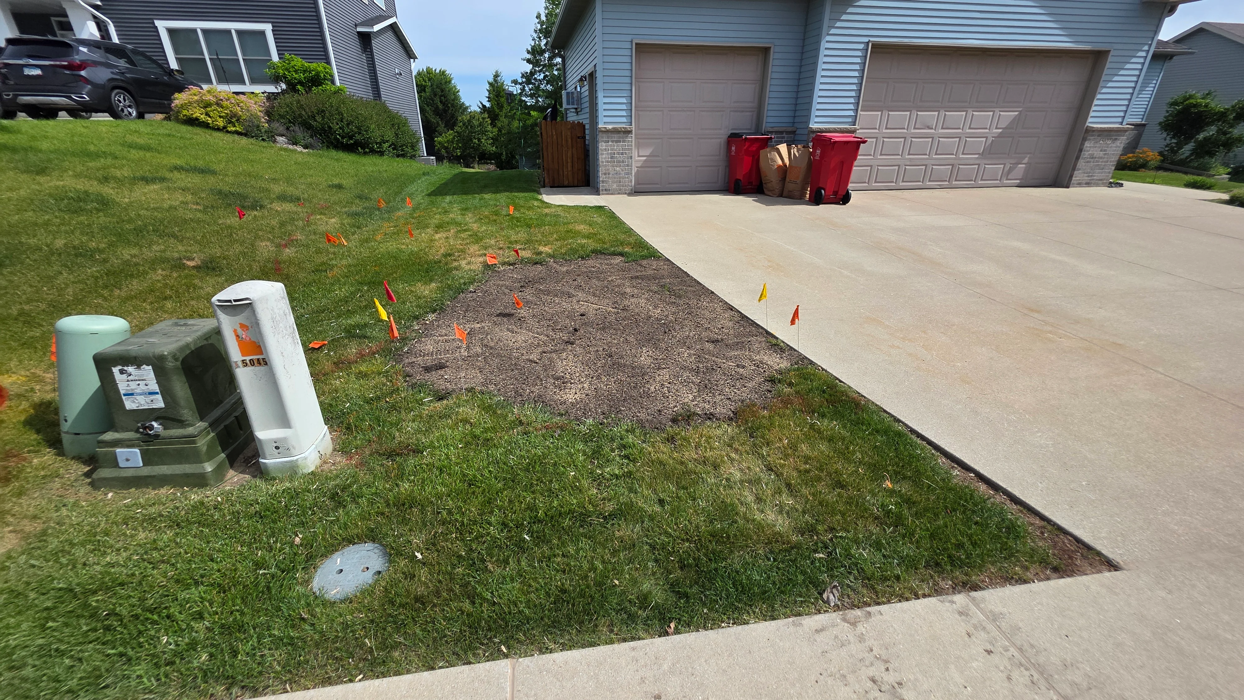 Utility line locating with colored flags marking underground gas, electric, and water lines before driveway work