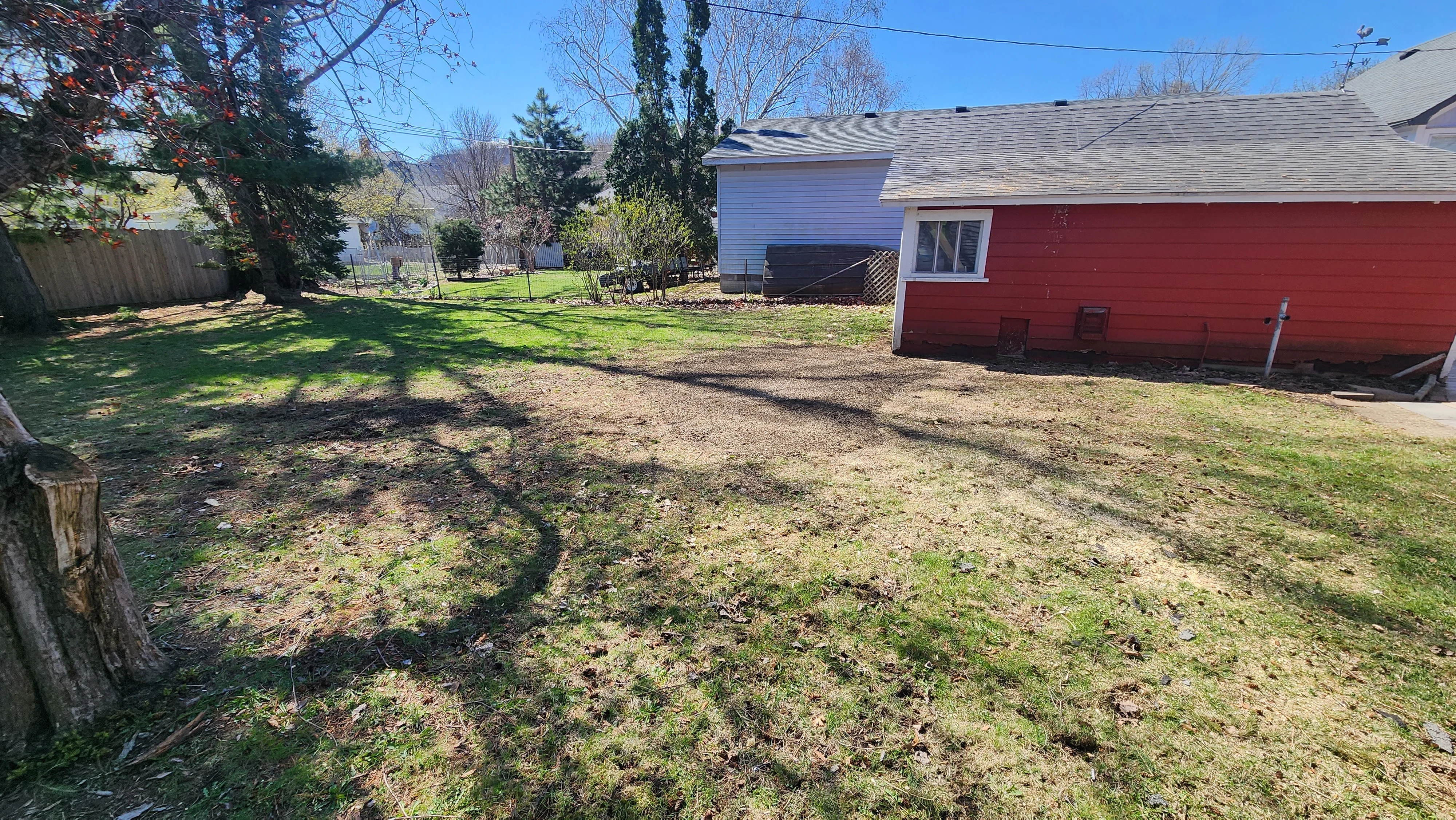 Cleared residential yard with graded soil, mature trees, and red outbuilding visible