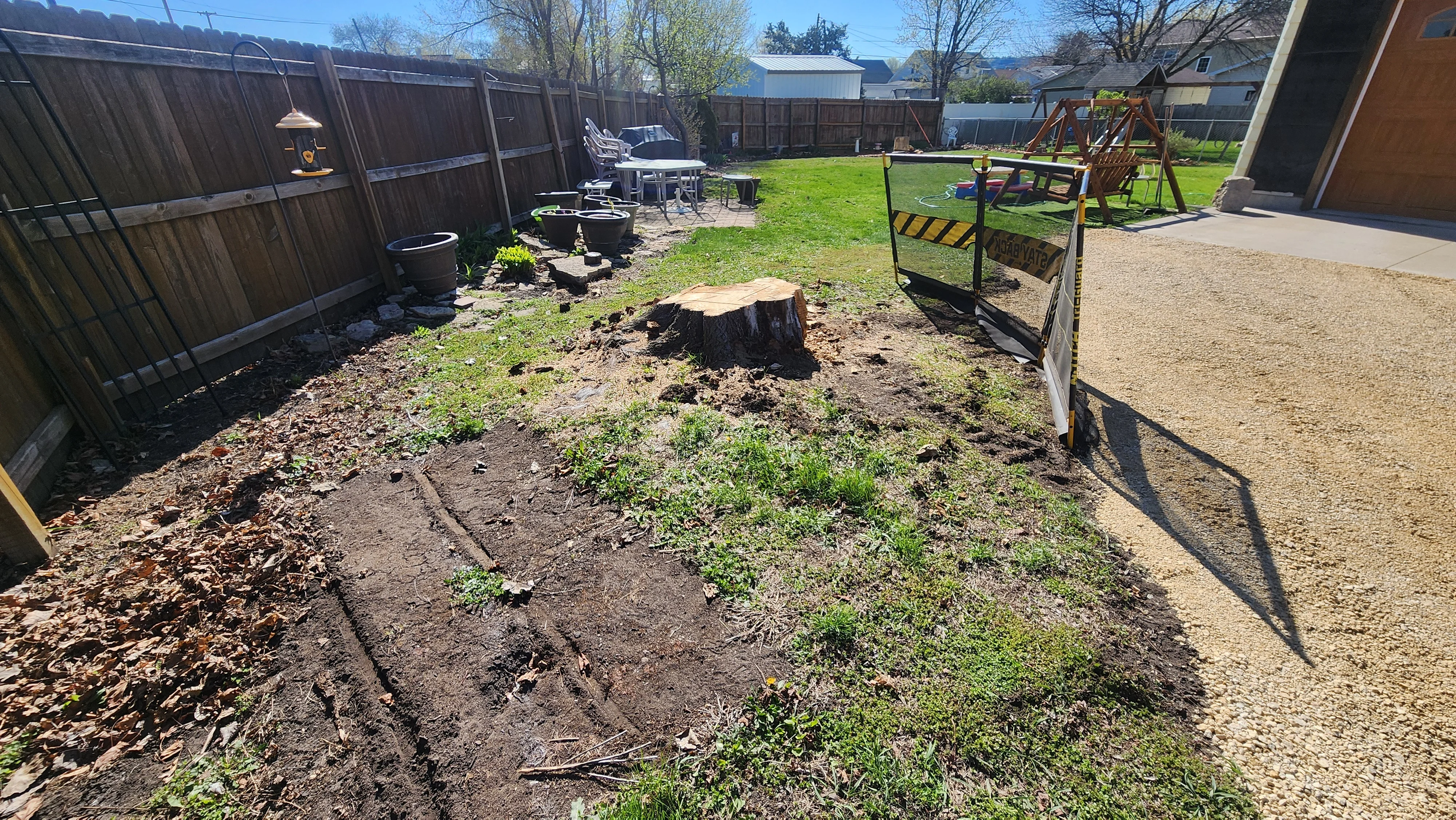 Removed tree stump in backyard with cleared soil and wood chips, fenced residential yard