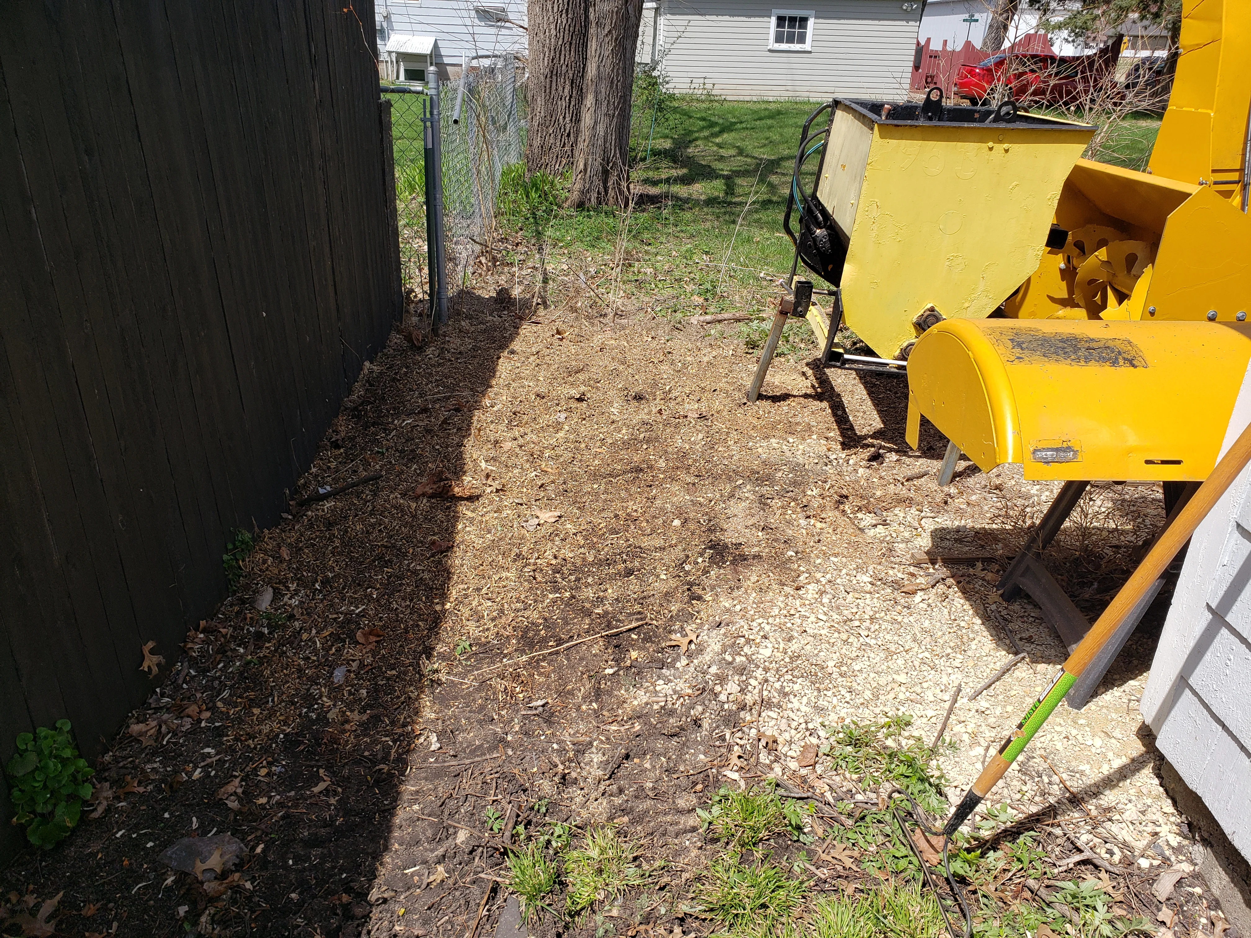 Fresh wood chip mulch applied along driveway and black fence line with yellow chipper equipment on site