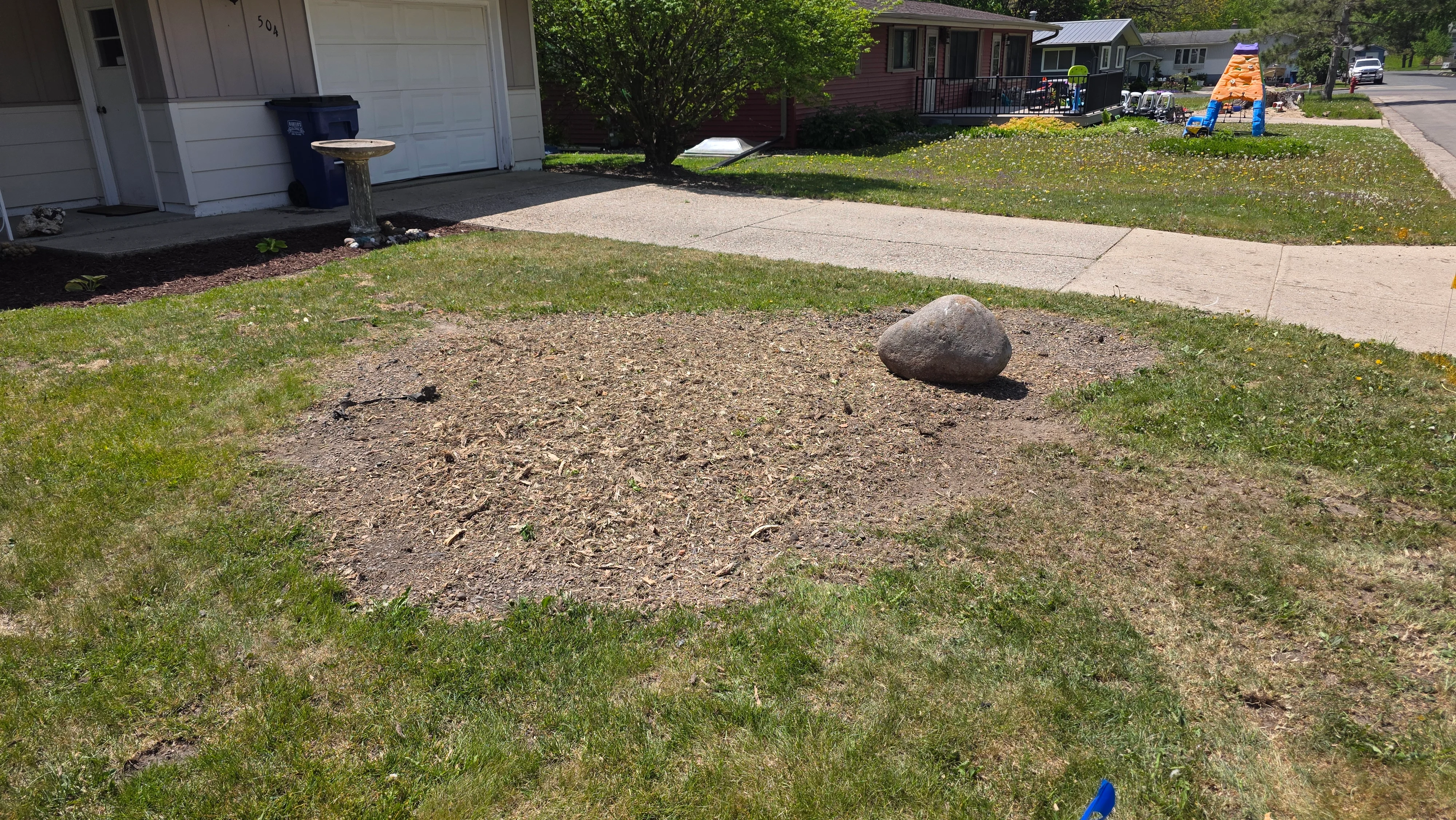 Cleared residential lot with graded soil, decorative boulder, and defined lawn edges